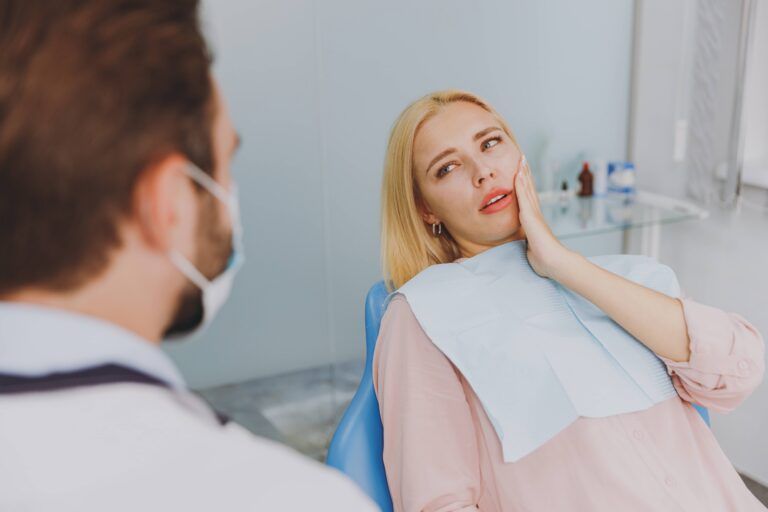 Young ill woman 20s look at dentist sit at office chair indoor light cabinet hold cheeck